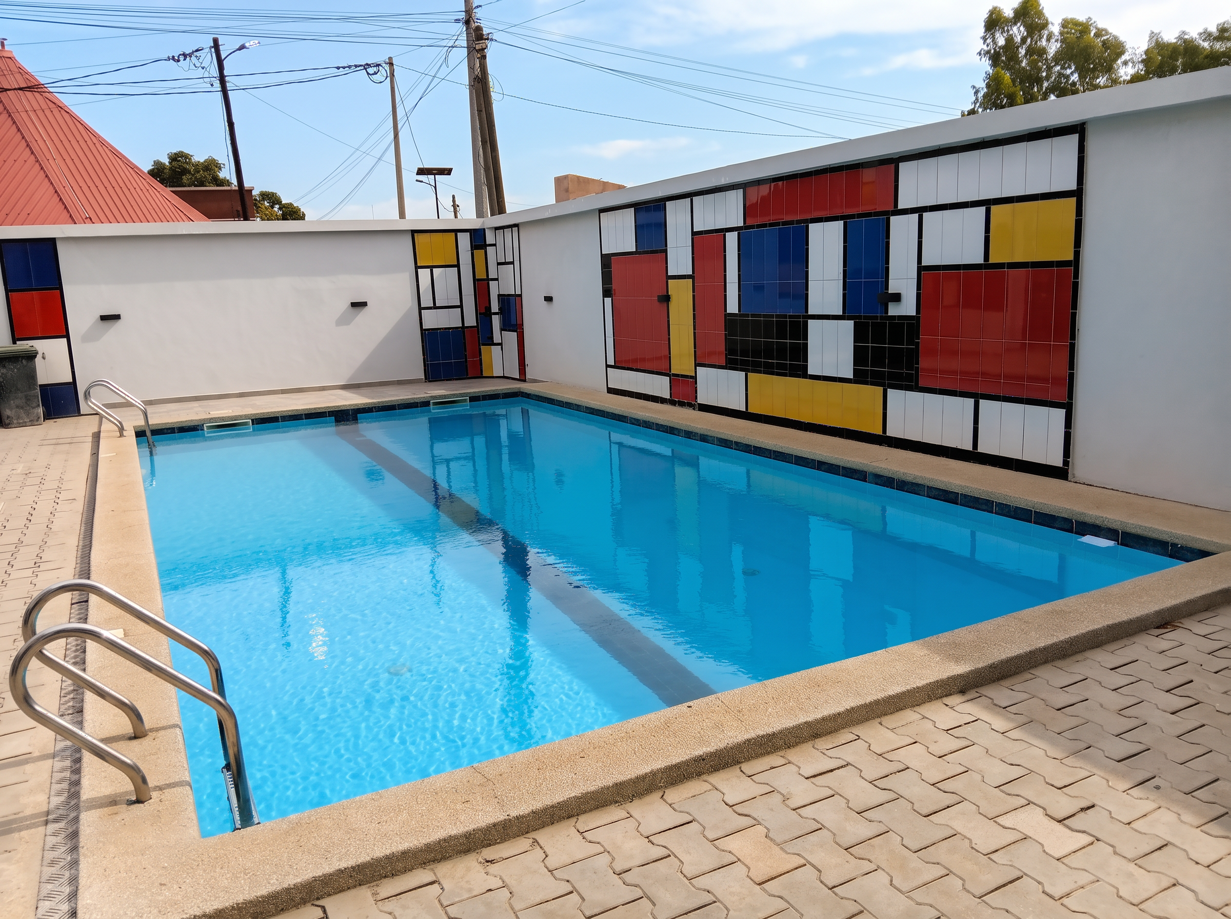 Bassin extérieur bordé par la fresque carrelée inspirée de Piet Mondrian sous le ciel de Saly Portudal