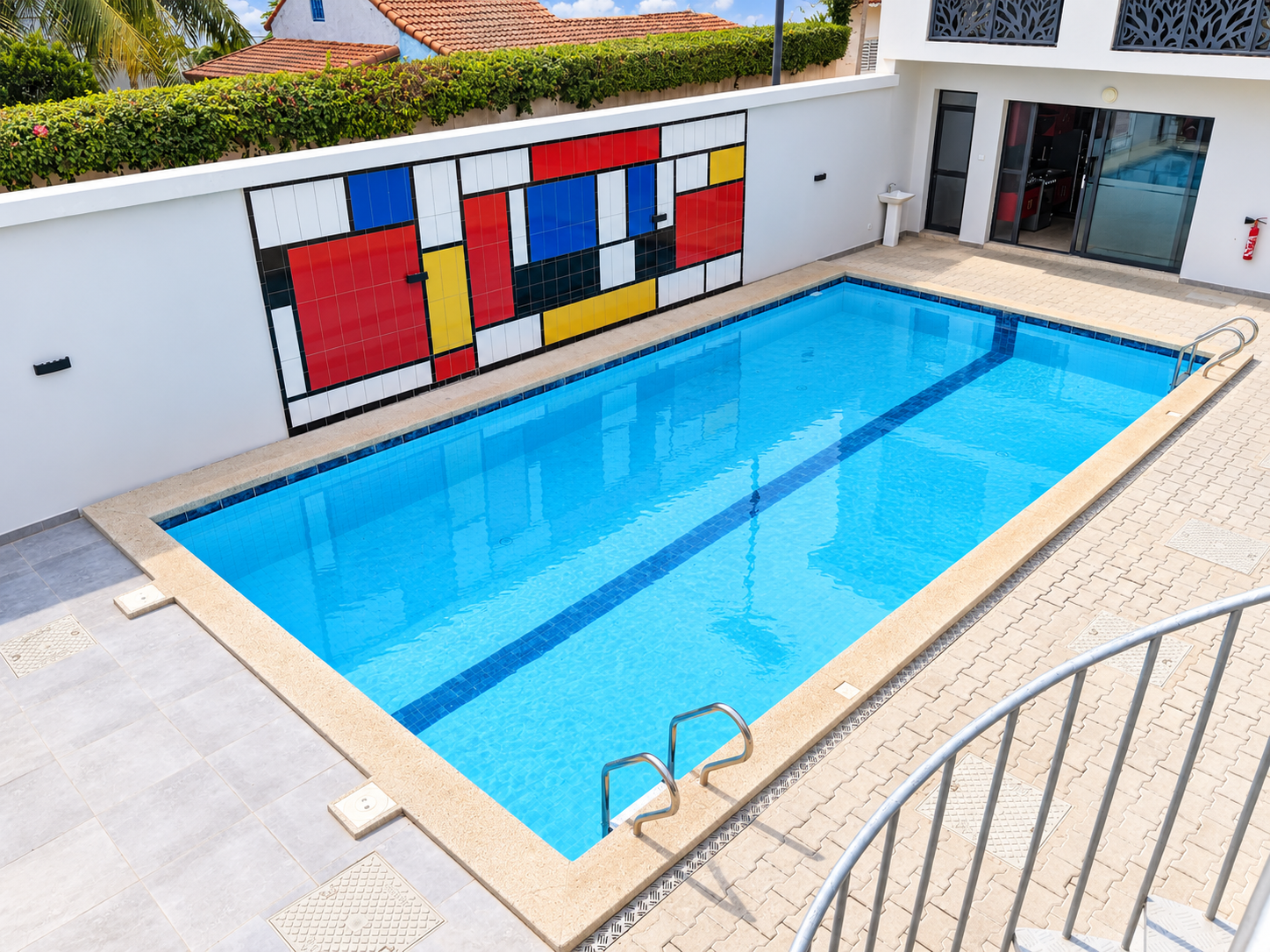 Vue plongeante sur la piscine extérieure du Mondrian et sa fresque murale géométrique rouge, bleue, jaune et blanche à Saly Portudal