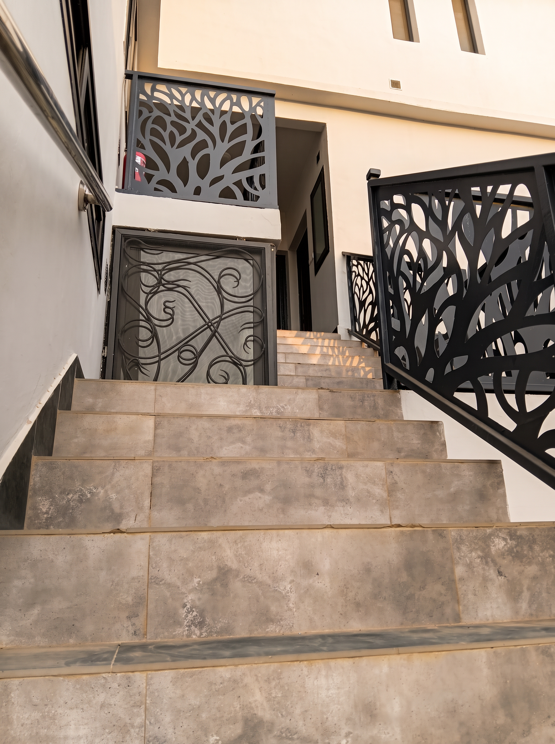 Escalier en pierre grise et garde-corps métalliques noirs finement ajourés menant aux étages