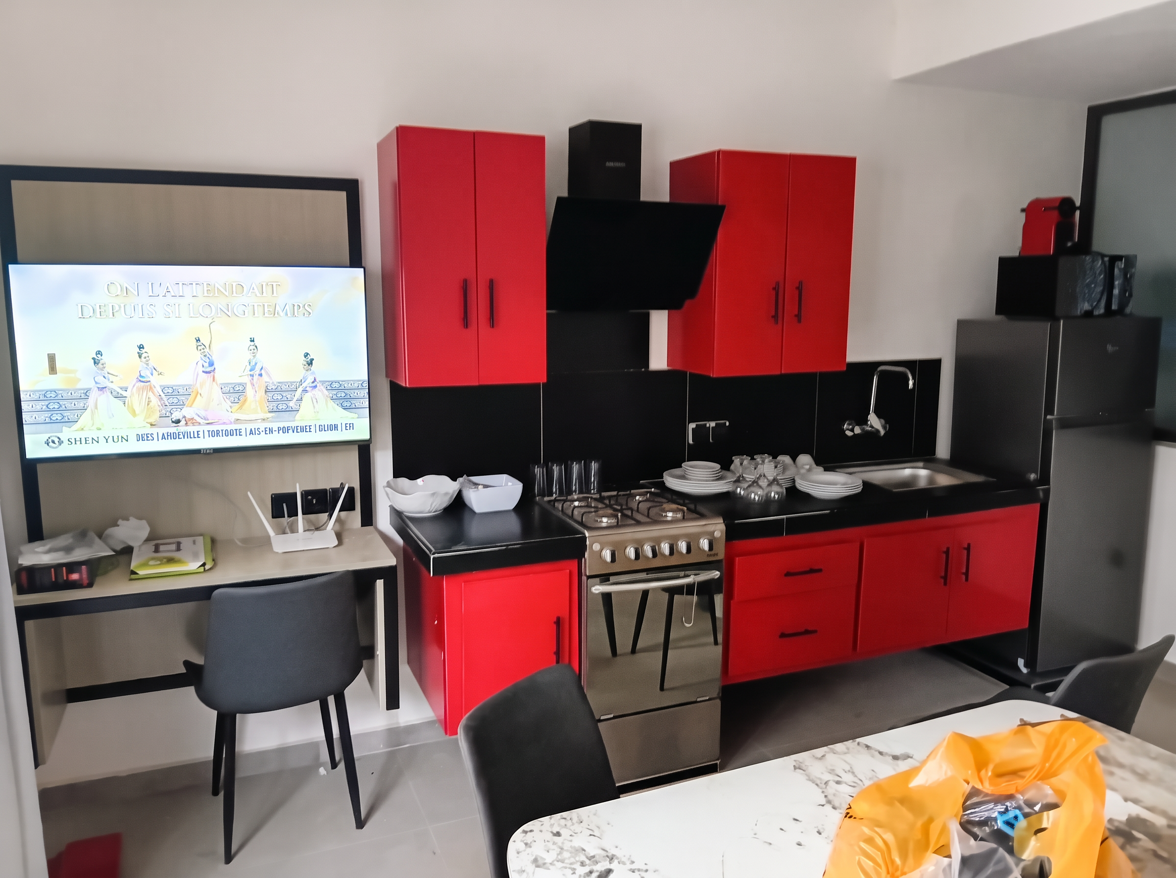 Espace intérieur avec coin cuisine rouge et noir et bureau équipé d'un téléviseur mural